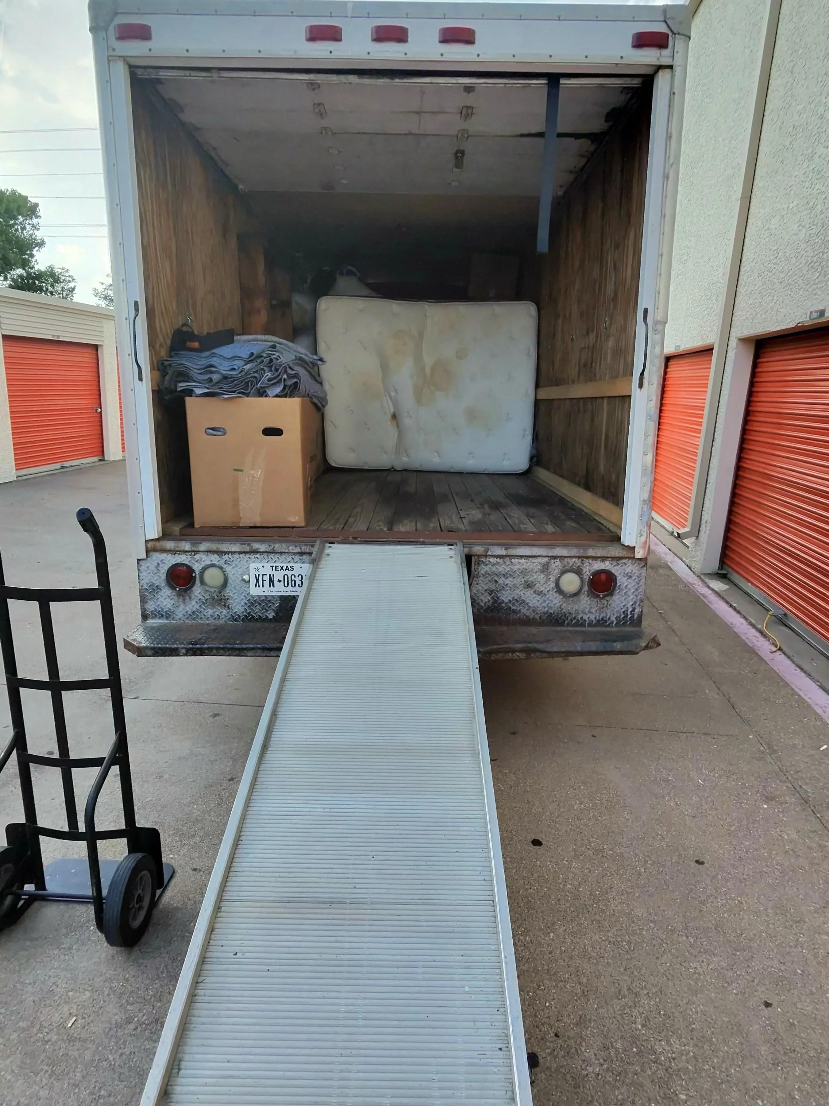 Moving truck with open cargo area loaded with boxes, mattress, and household furniture items