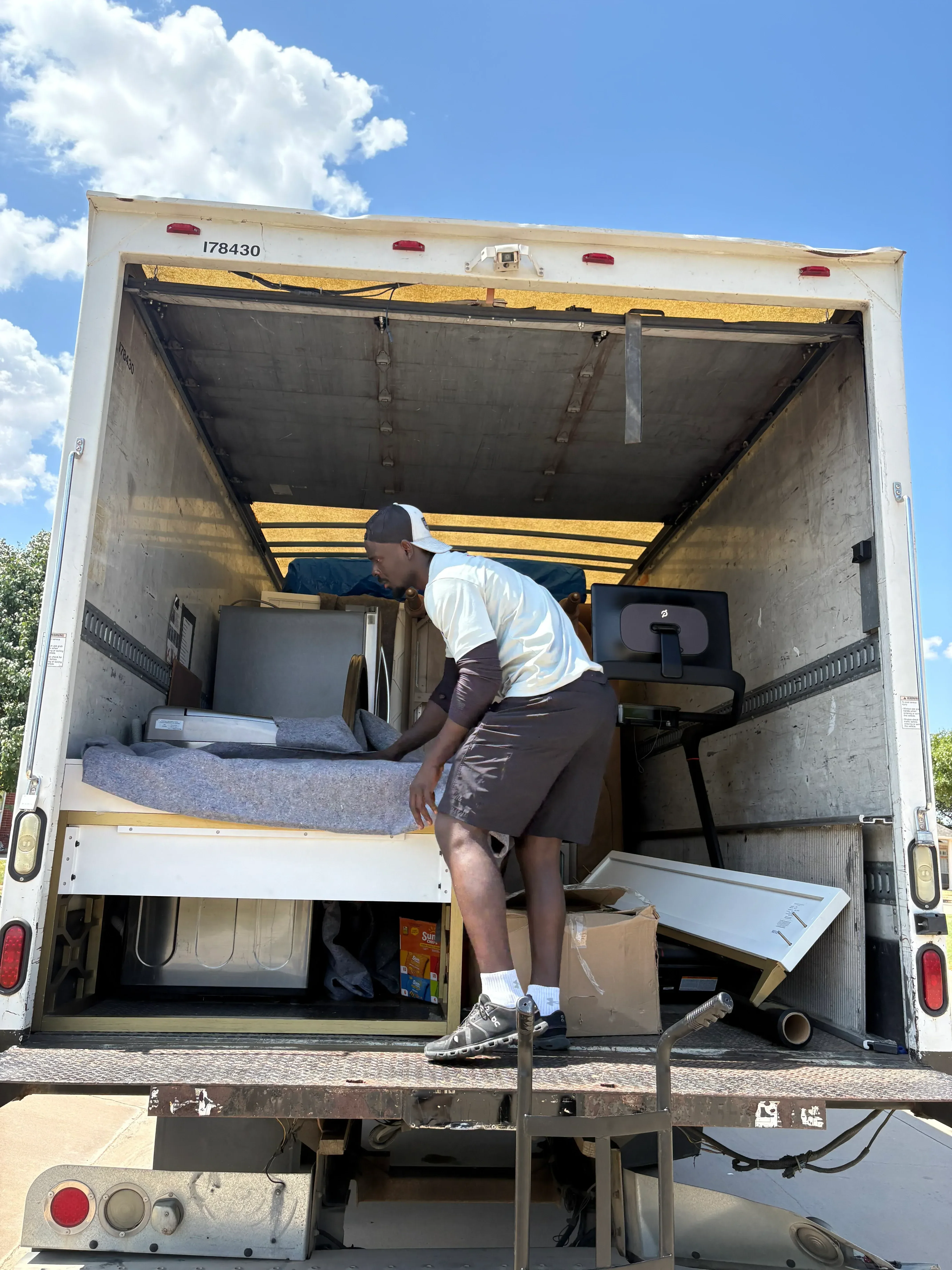 Moving crew loading furniture and household items into enclosed moving truck with yellow and white exterior