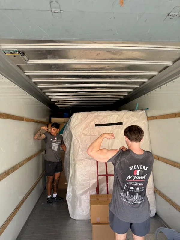 Moving crew loading wrapped furniture and boxes into truck interior with protective padding