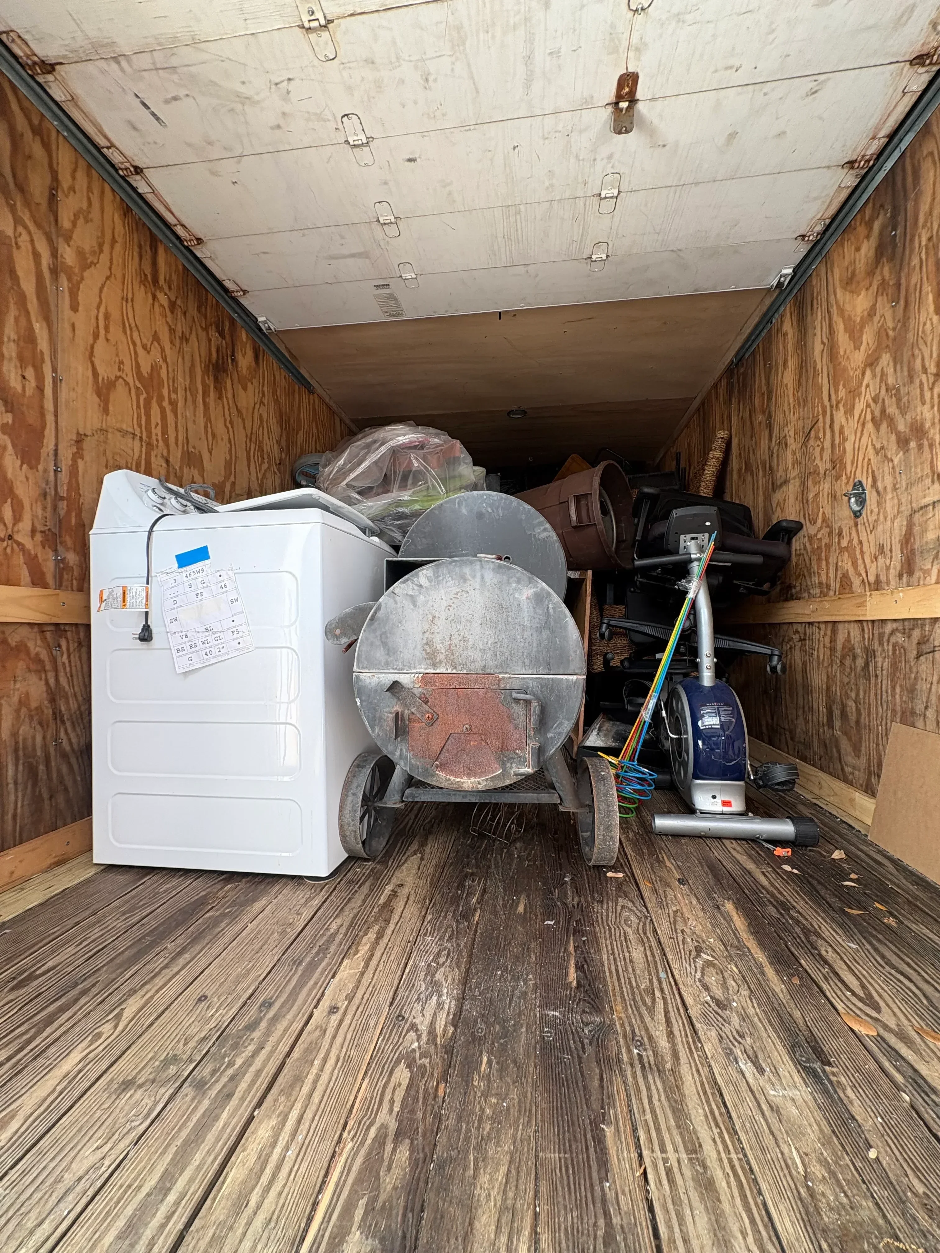 White washer and dryer unit secured in moving truck bed with household items and equipment