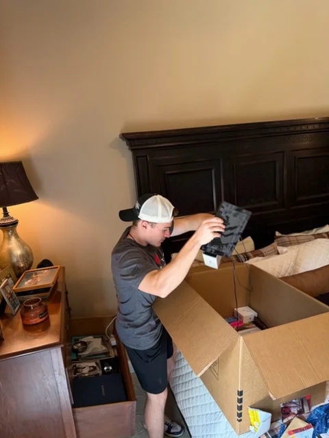 Moving crew member packing household items and clothing into cardboard boxes