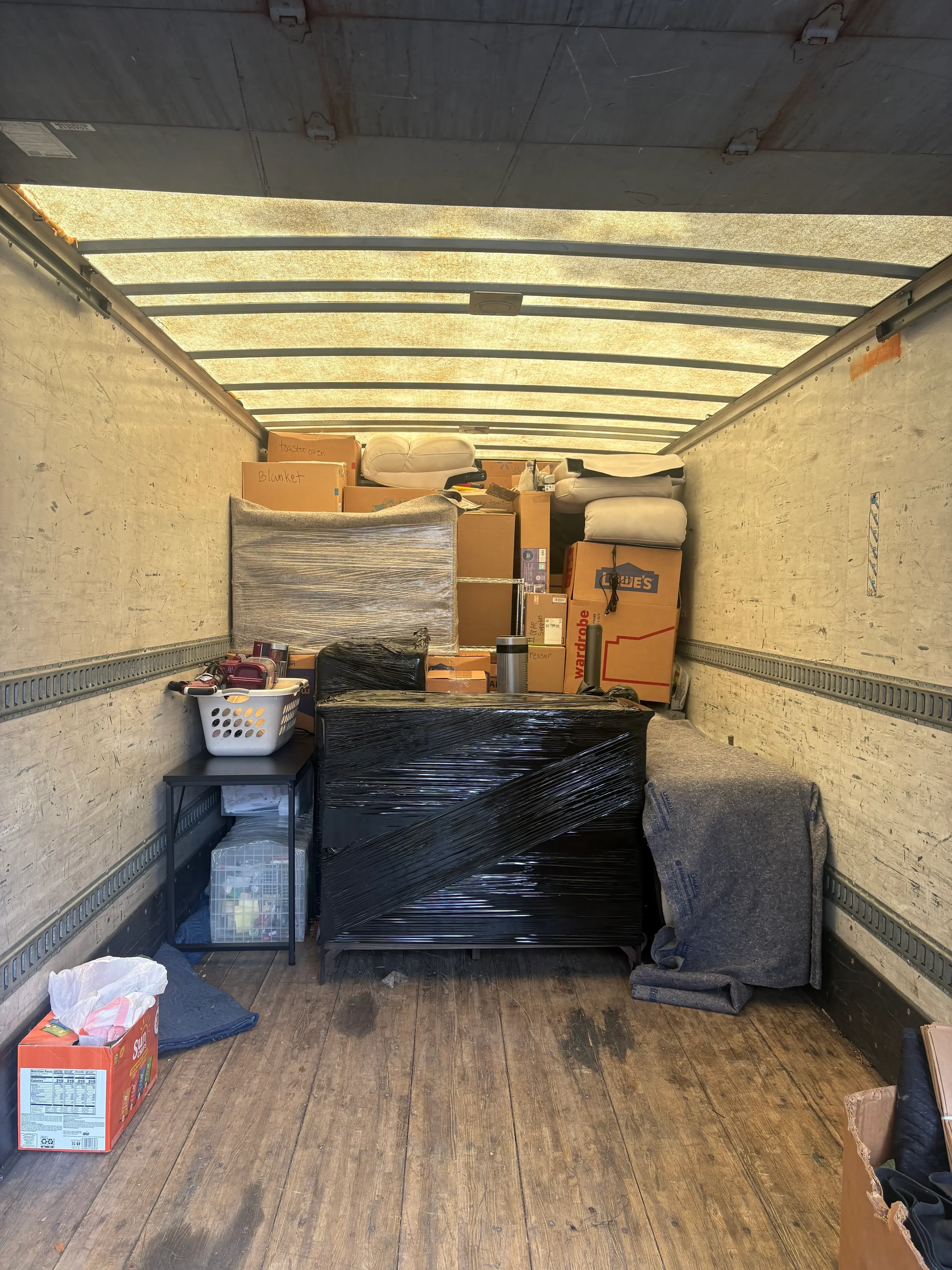 Moving truck interior with packed boxes, furniture, and household items secured with metal tie-downs