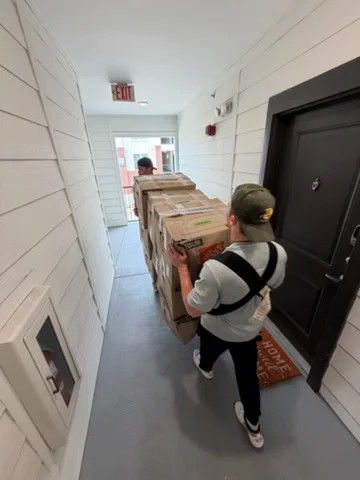 Moving crew transporting stacked boxes through narrow commercial corridor with white tile walls
